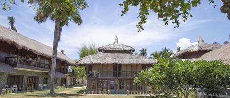 Un resort con edificios de techo de paja, una estructura central con cúpula y un césped bien cuidado.