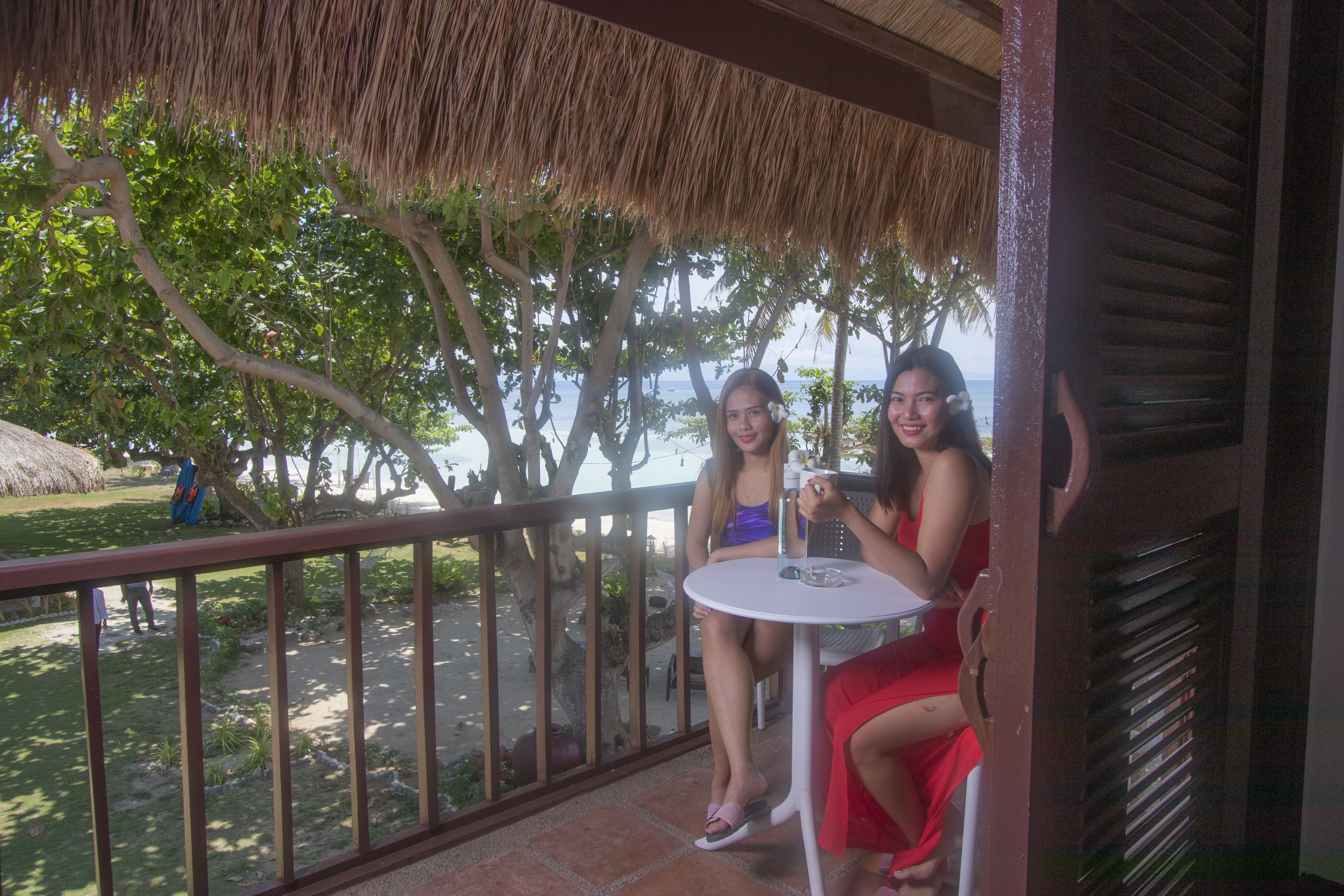 A balcony with a view of the sea, a thatched roof, and a white table.