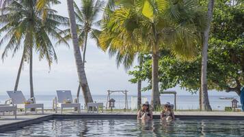 A poolside area with lounge chairs, palm trees, and a view of the ocean.