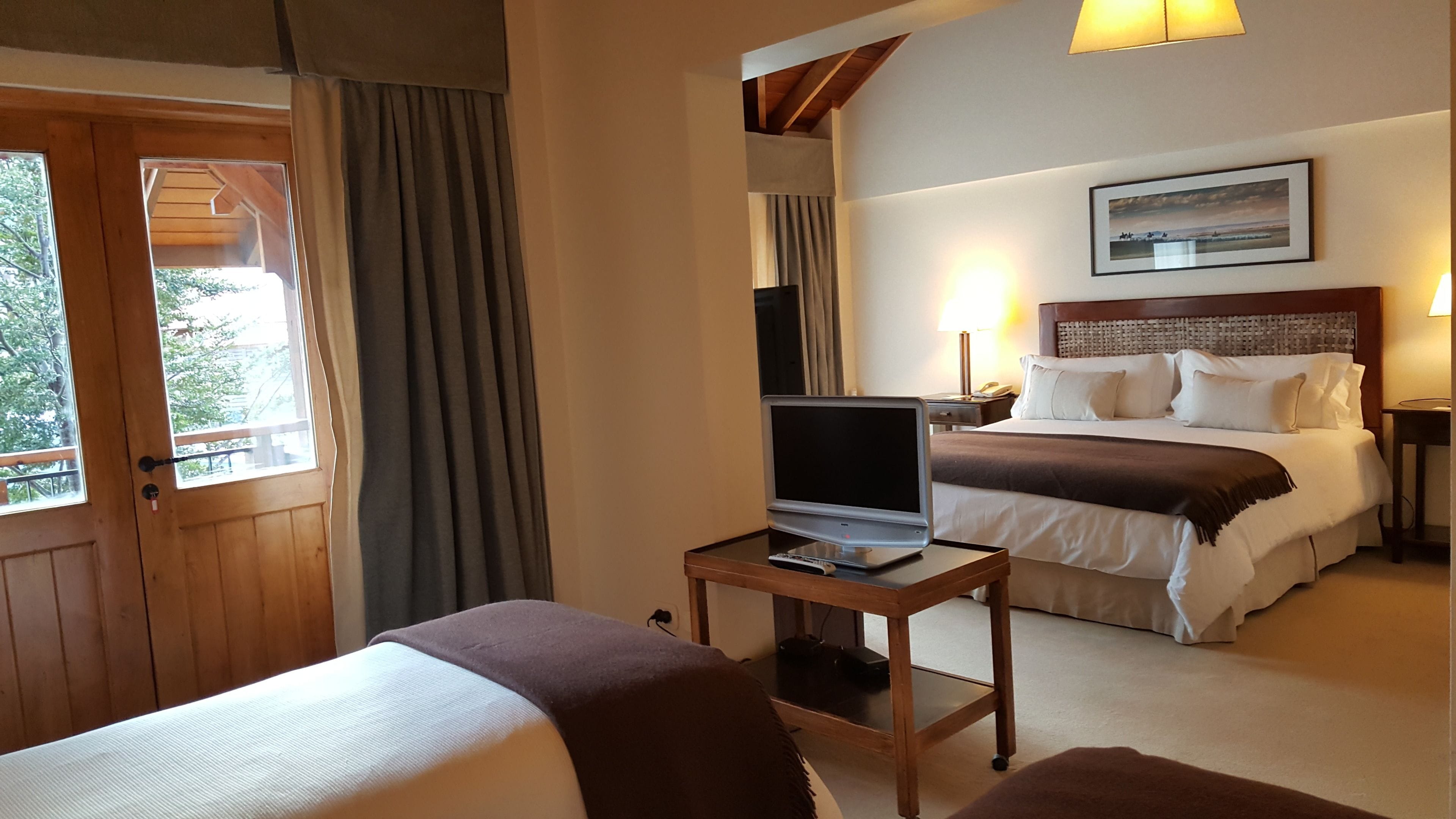 Habitación de hotel con cama, escritorio con computadora portátil, ventana y un cuadro en la pared.
