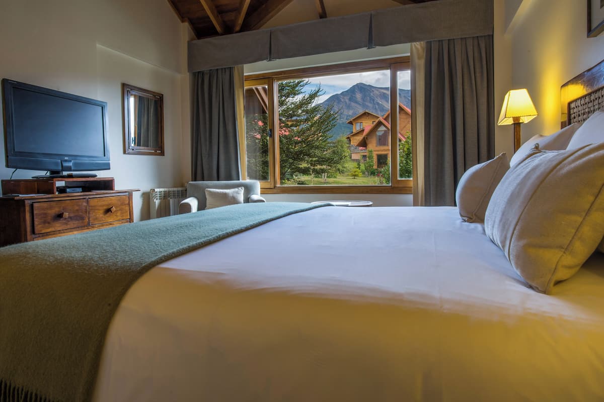 Una habitación de hotel con una cama grande, televisión, una silla y vistas a las montañas.