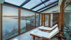 Una habitación iluminada por el sol con amplias ventanas de vidrio que dan a un lago y montañas.