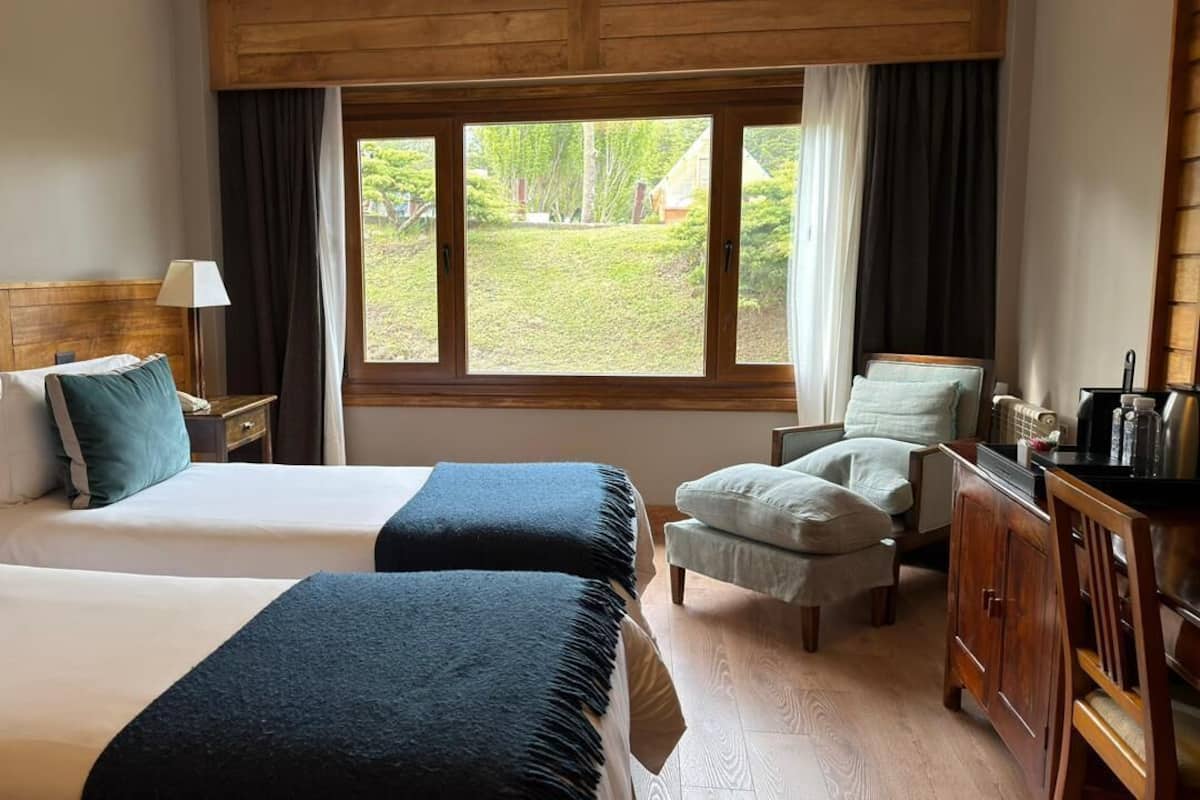 Una habitación de hotel con dos camas, un escritorio, una silla y vistas al exterior.