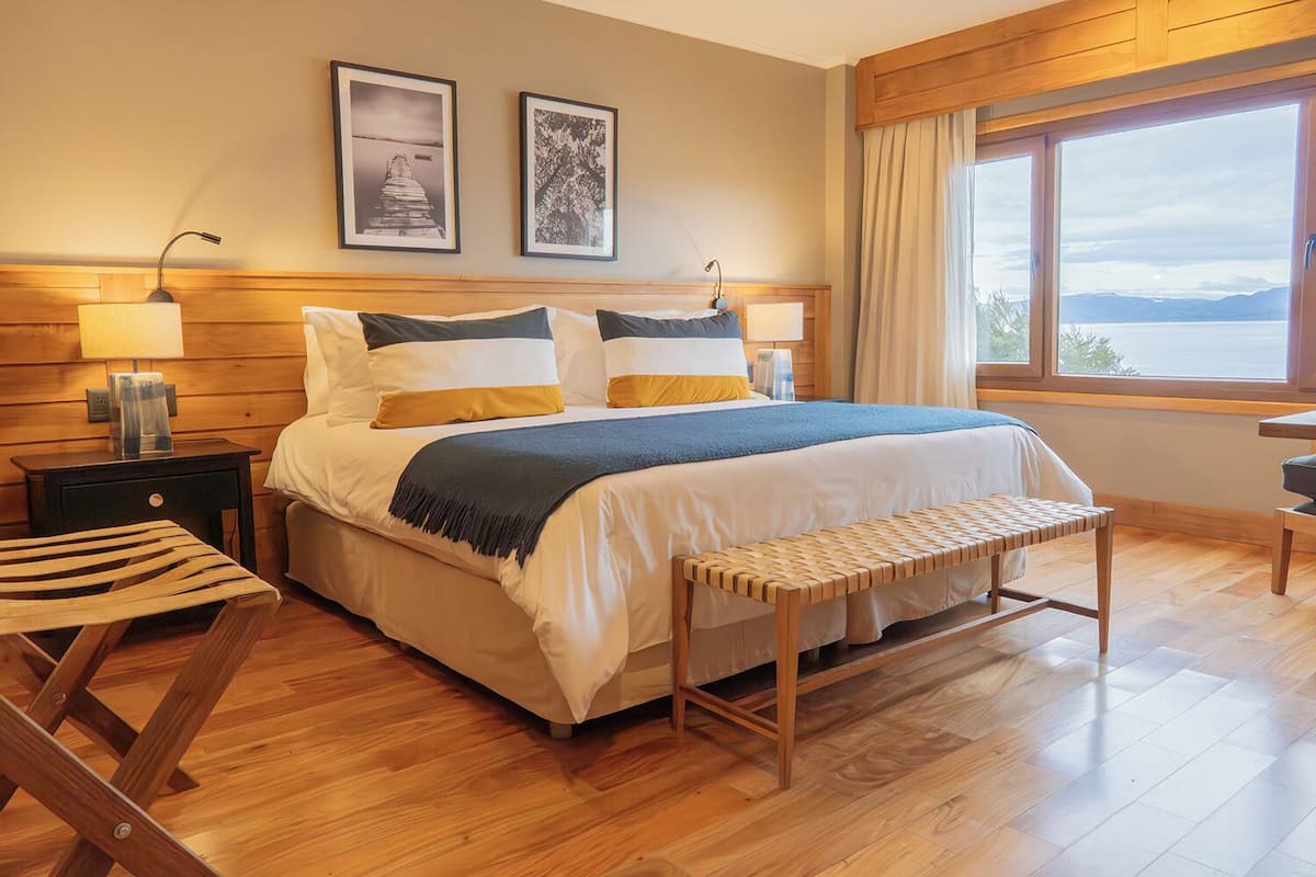 Un dormitorio ordenado con cama, mesitas de noche, un banco y una ventana con vistas.