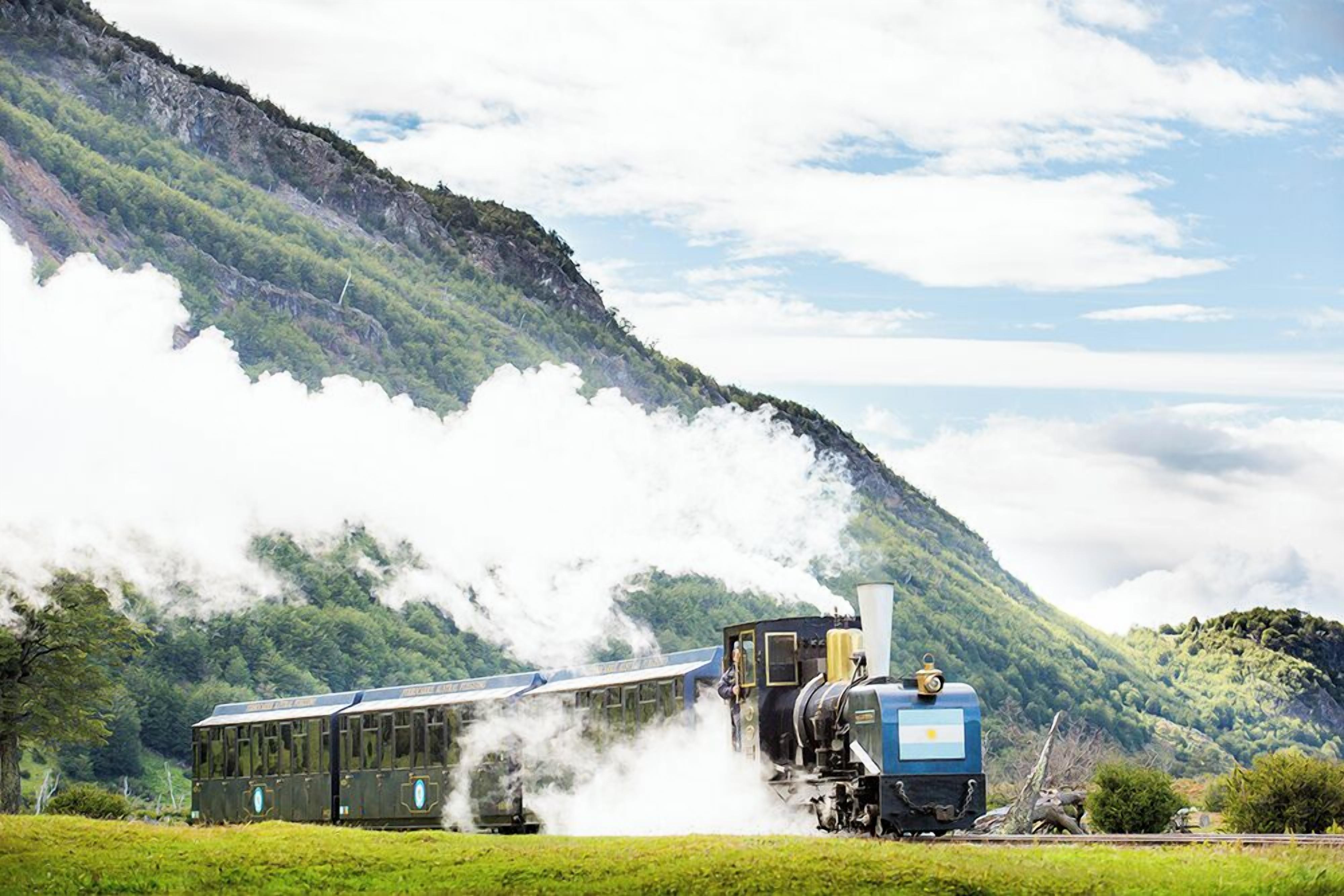 A steam train with a blue locomotive pulling passenger cars through a mountainous landscape.