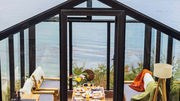 Un comedor con techo de cristal, una mesa para dos, vistas a un cuerpo de agua y montañas.