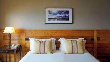 A hotel room with a wooden headboard, a bed with white linens, two striped pillows, a bedside table with a lamp and a phone, and a framed picture on the wall.