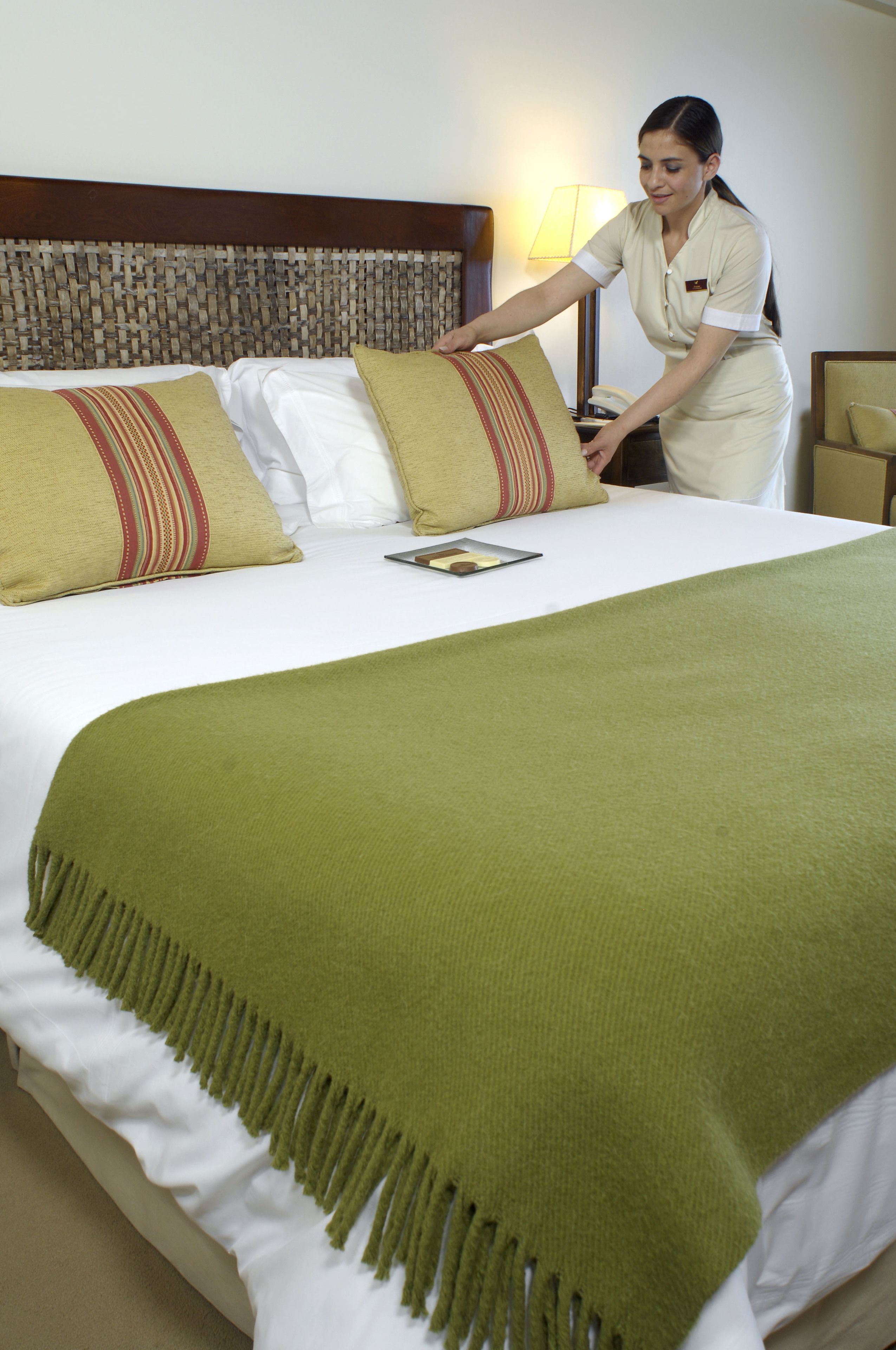 A neatly made bed with a green throw blanket, white pillows, and a striped pillow.