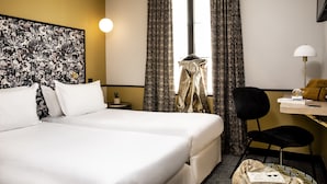 A hotel room with two beds, a desk with a lamp, a chair, and a window with curtains. - Hotel Paris La Fayette (Paris)