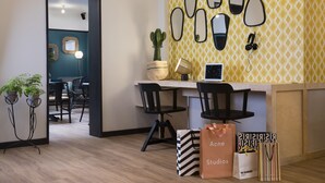 A modern kitchen with a yellow patterned backsplash, black chairs, and a dining table. There are potted plants, a laptop, and gift bags on the counter. - Hotel Paris La Fayette (Paris)