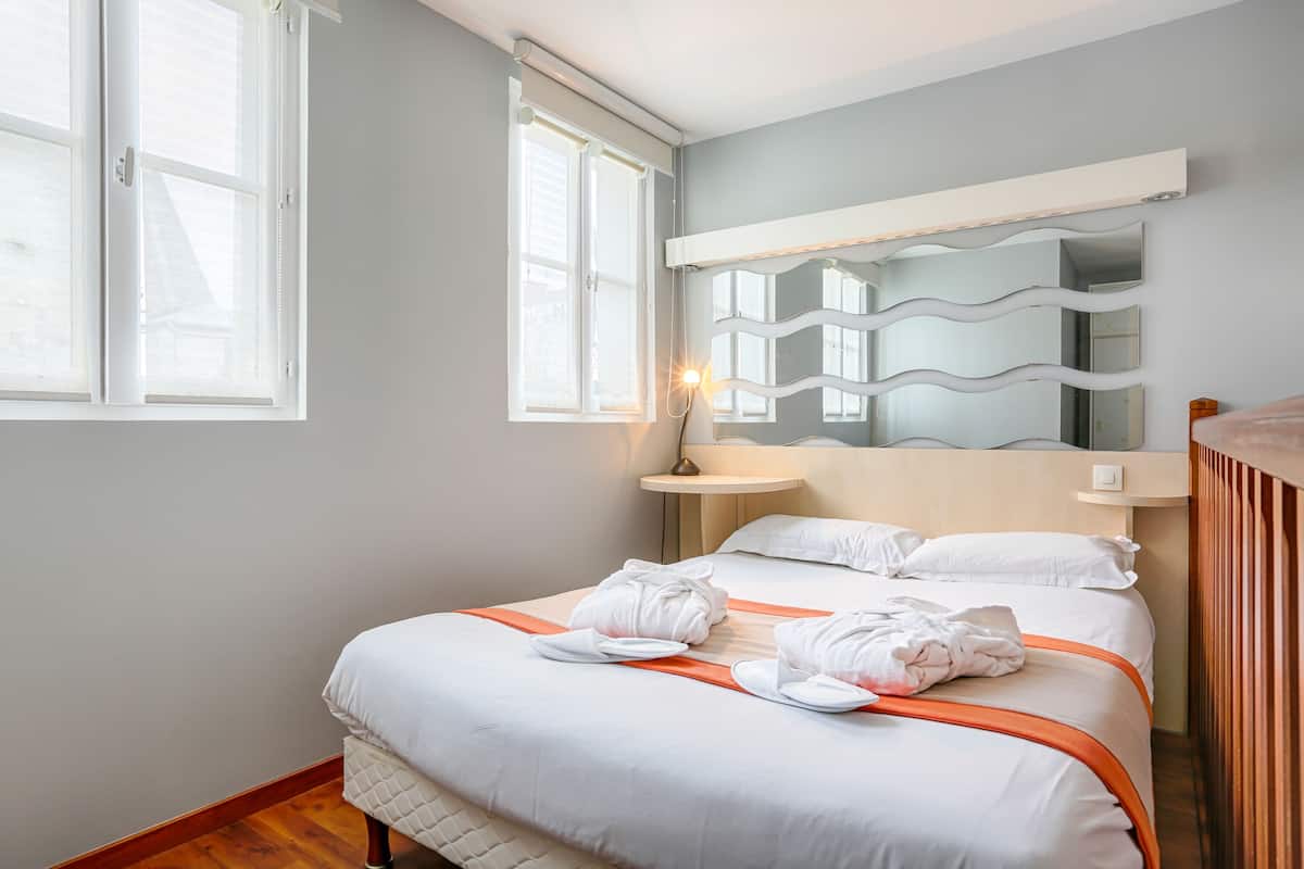 A hotel room with a bed, a bedside table, a mirror, and a window.