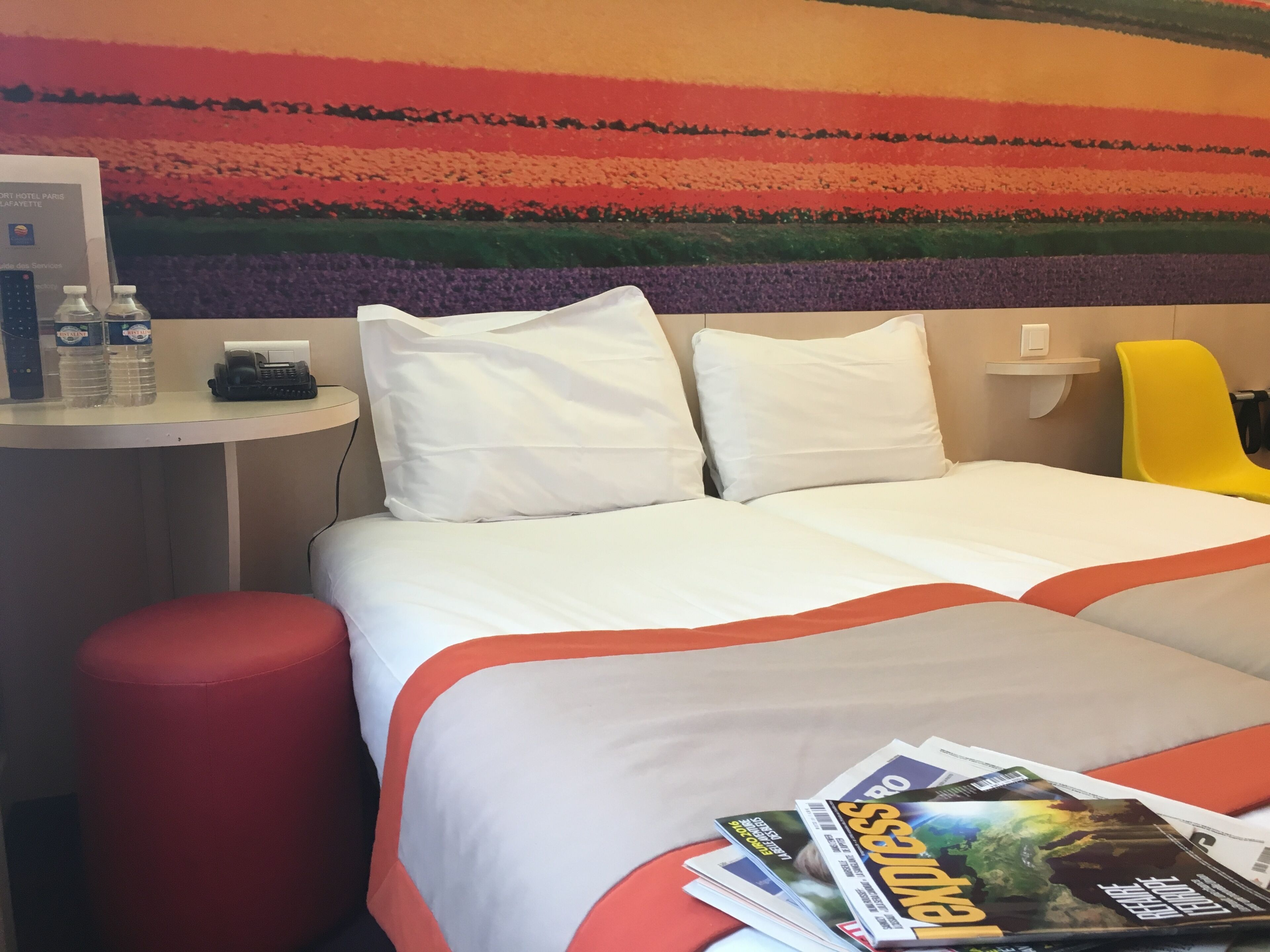 A hotel room with a bed, a desk with a telephone, a chair, and a magazine on the bed.