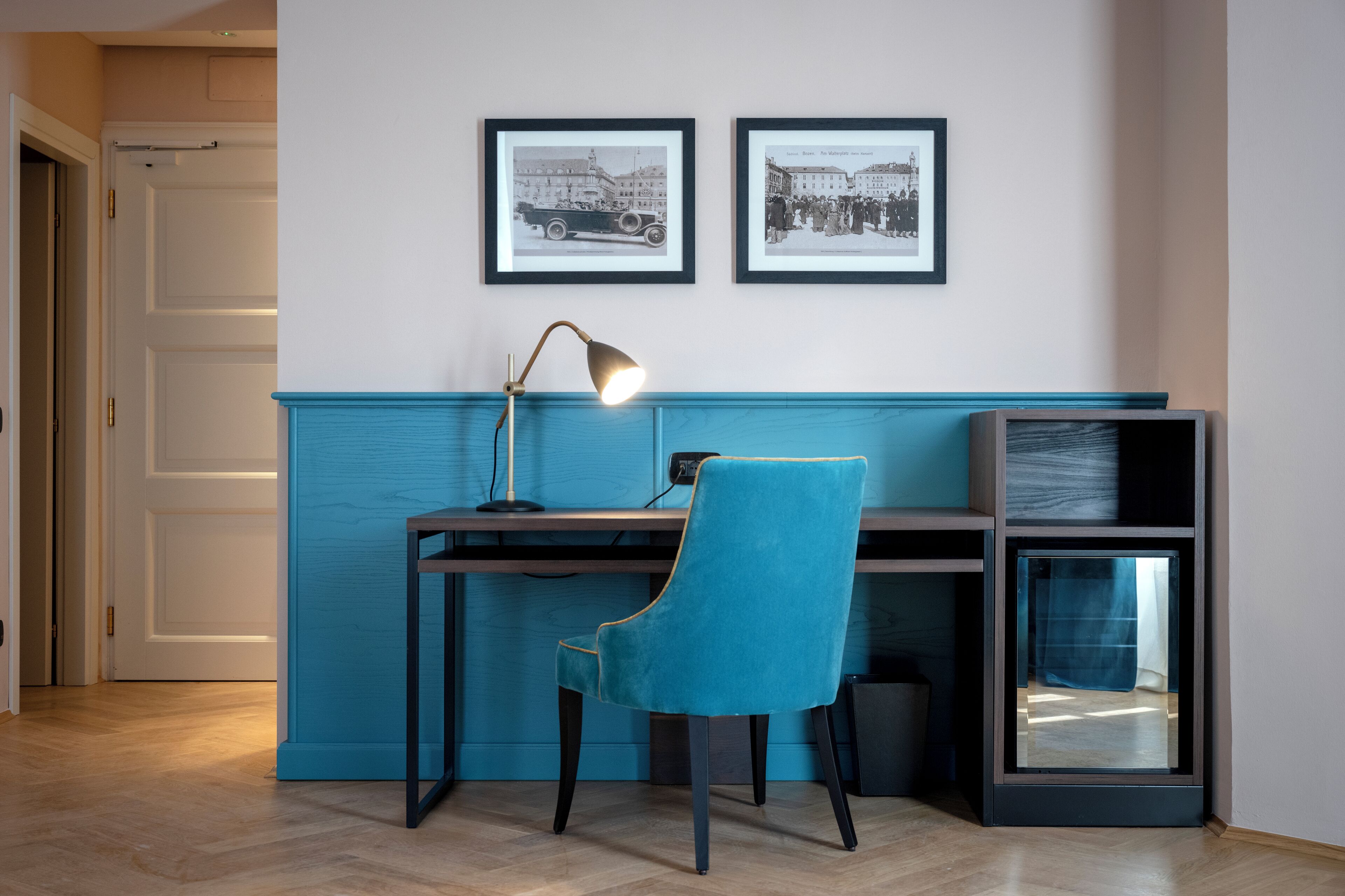 Ein Zimmer mit einem Schreibtisch, einem Stuhl und zwei gerahmten Fotografien an der Wand.