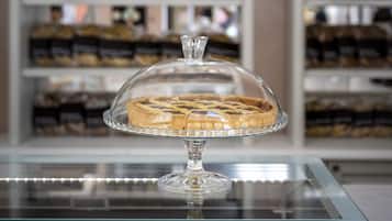 Una vitrina de pastelería con un pastel sobre un pedestal de vidrio, repisas con productos horneados al fondo y ventanas arqueadas.