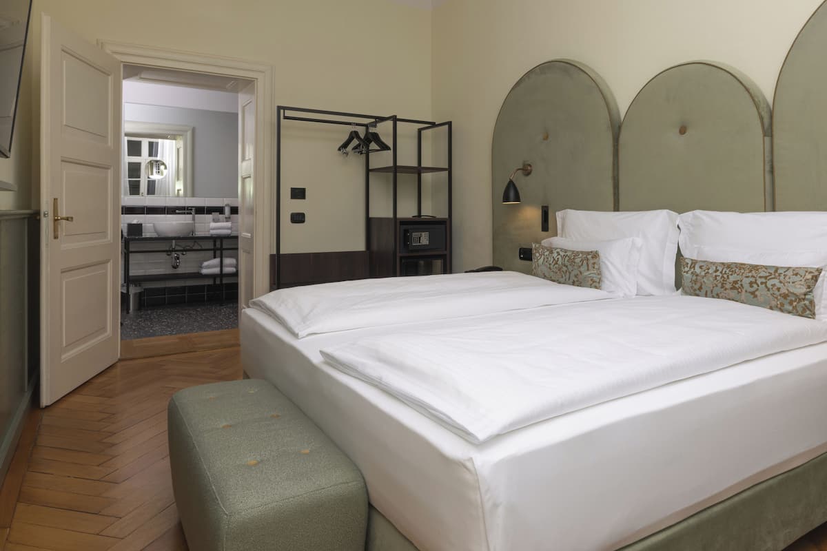 A neatly arranged hotel room with a large bed, a bench, a wardrobe, and a bathroom visible through an open door.