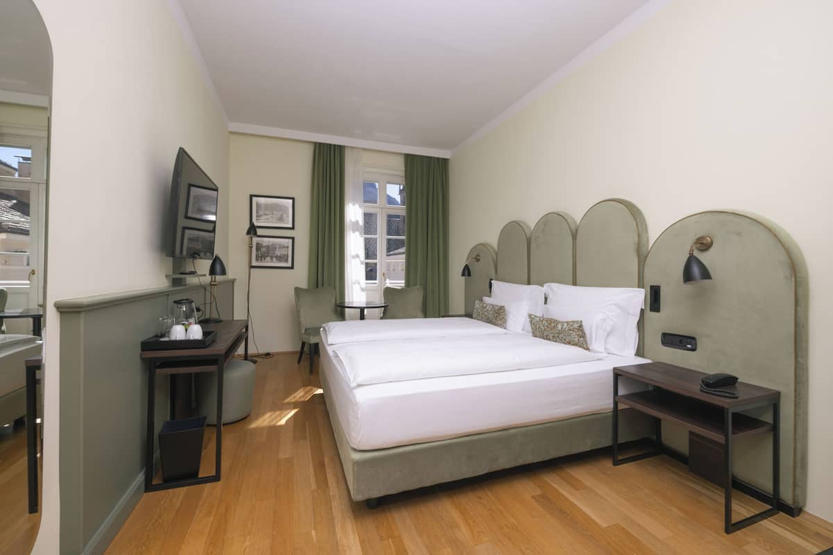 A hotel room with a bed, bedside tables, a desk, a chair, and a window with curtains.