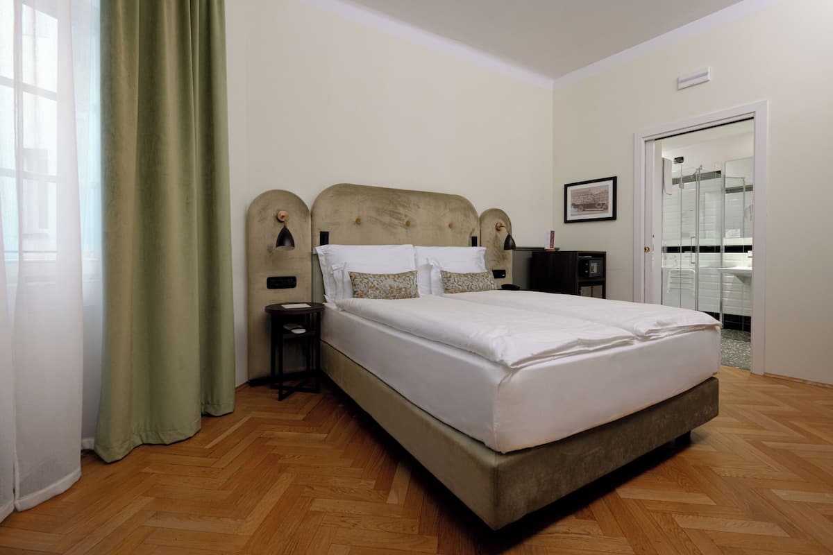 A hotel room with a bed, a nightstand, a lamp, a door, and a window with curtains.