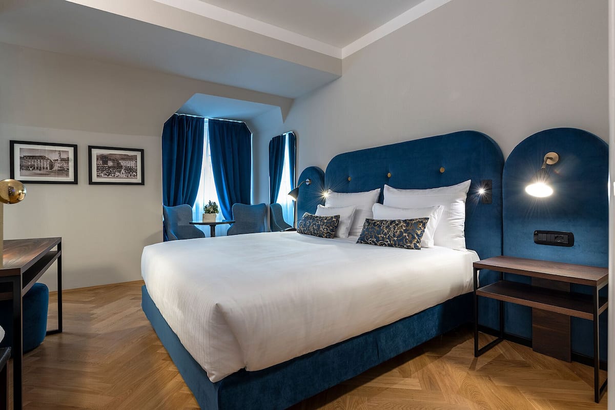 A bedroom with a large bed, a desk, a chair, and two framed pictures on the wall.