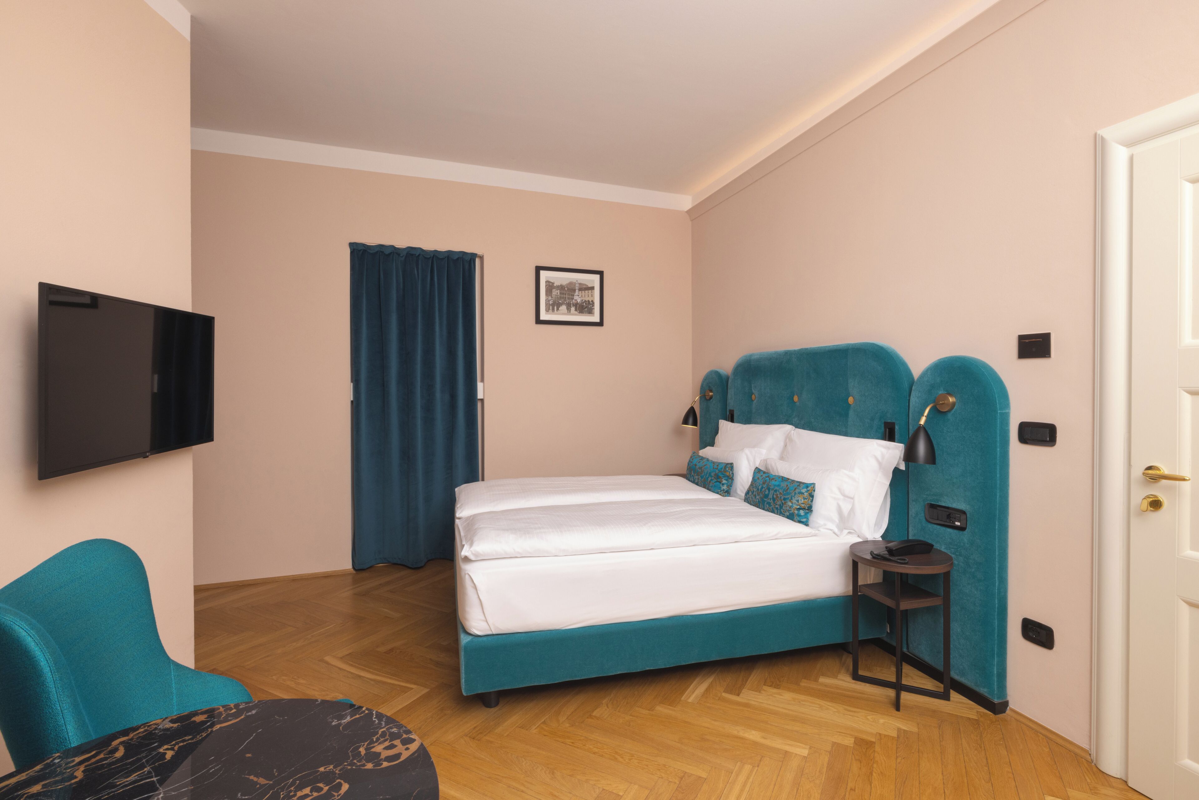 A bedroom with a bed, a chair, a small table, a TV, and a door.