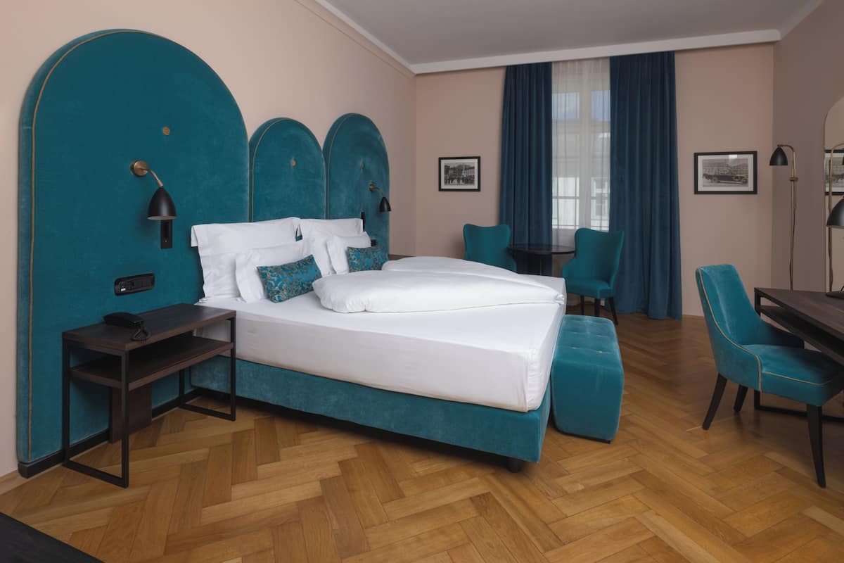 A hotel room with a large bed, a desk, a chair, and a small table.