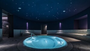 A modern indoor swimming pool with a starry ceiling, surrounded by stone walls and minimalist design. - Stadt Hotel Citta (Bolzano)