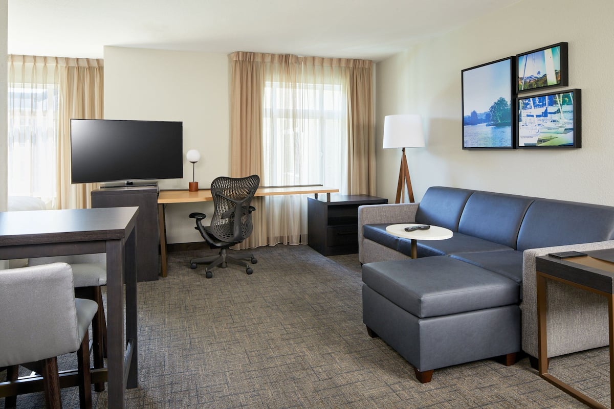 A hotel room with a flat-screen TV, a desk with a computer, a sofa, and a small table.