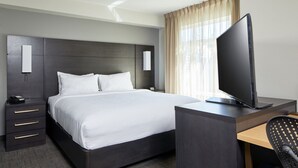 A hotel room with a bed, a desk with a computer, a chair, a telephone, and a TV.