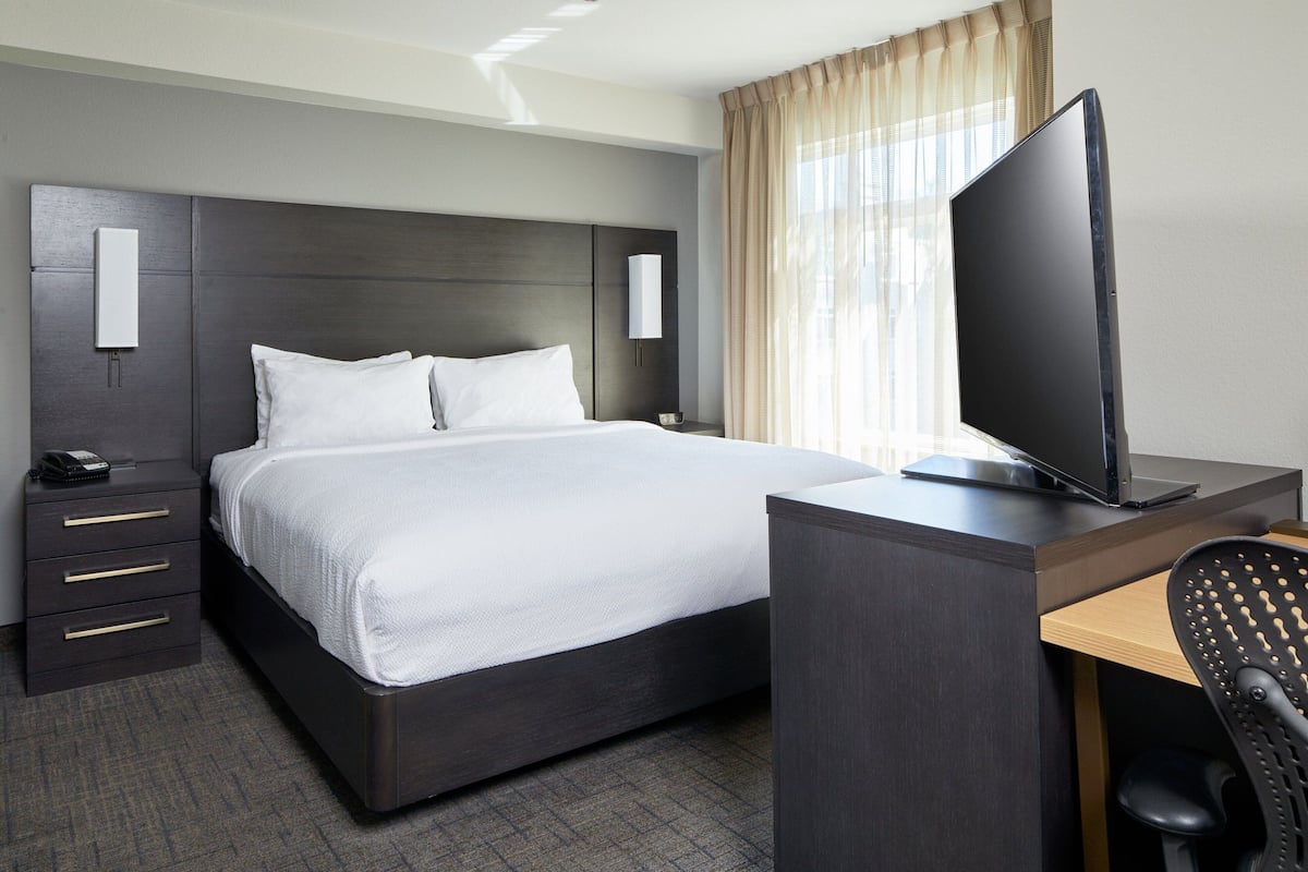 A hotel room with a bed, a desk with a computer, a chair, a telephone, and a TV.