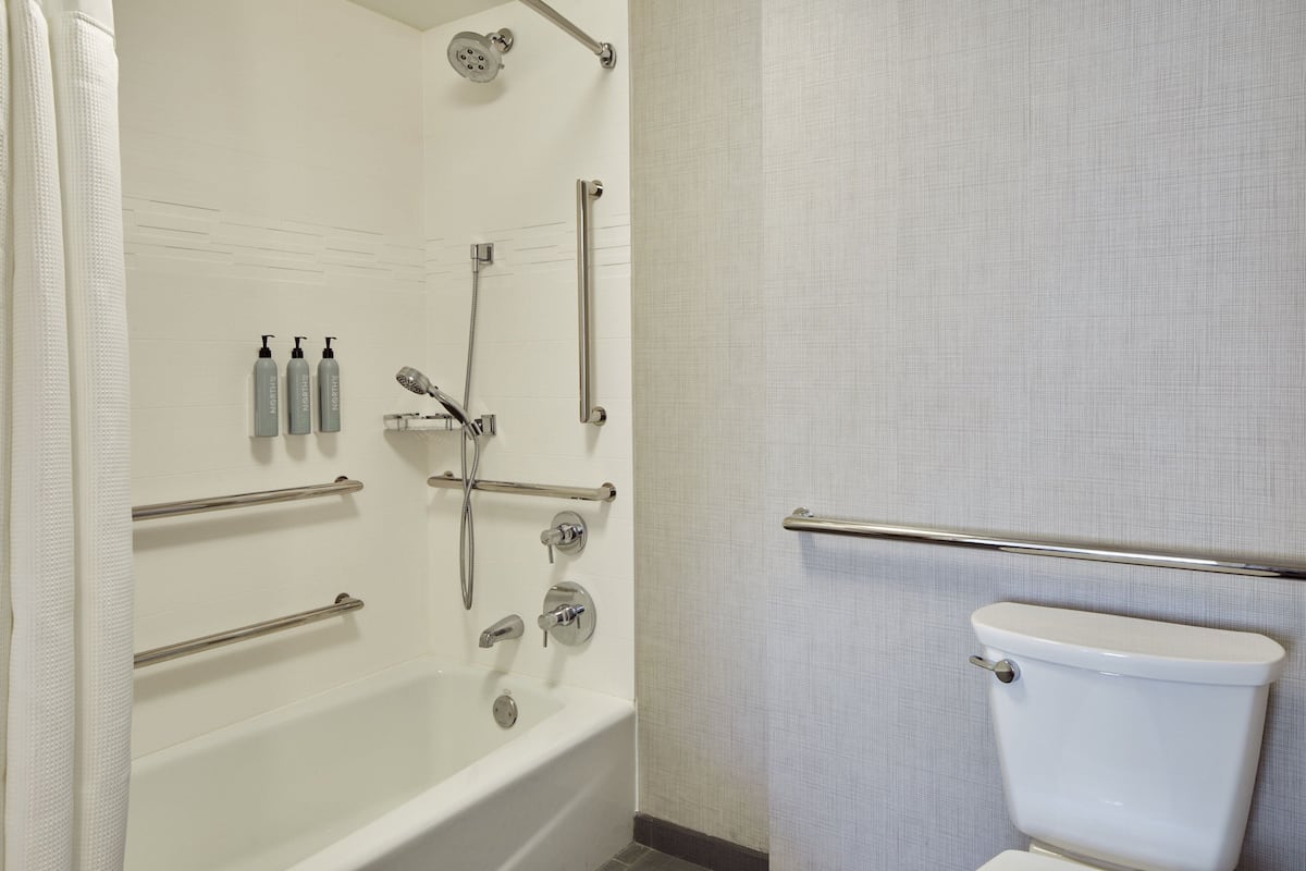 A bathroom with a bathtub, shower, and toilet. There are handrails and a grab bar for safety.