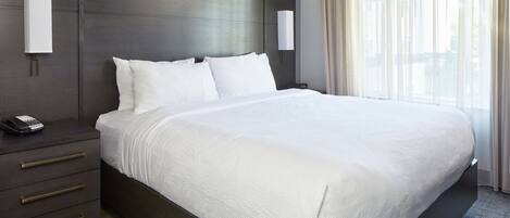 A modern hotel room with a large bed, a bedside table with a phone, and a nightstand.