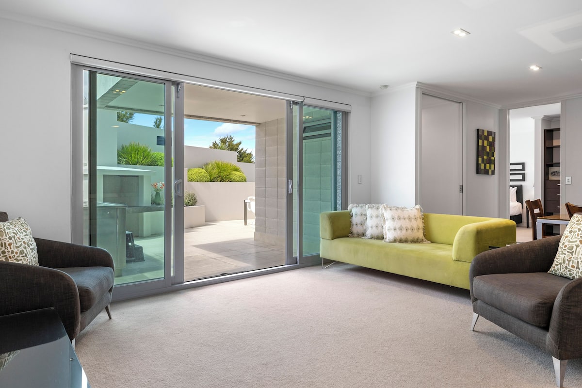 A modern living room with a sliding glass door leading to a balcony, a yellow sofa, and two armchairs.