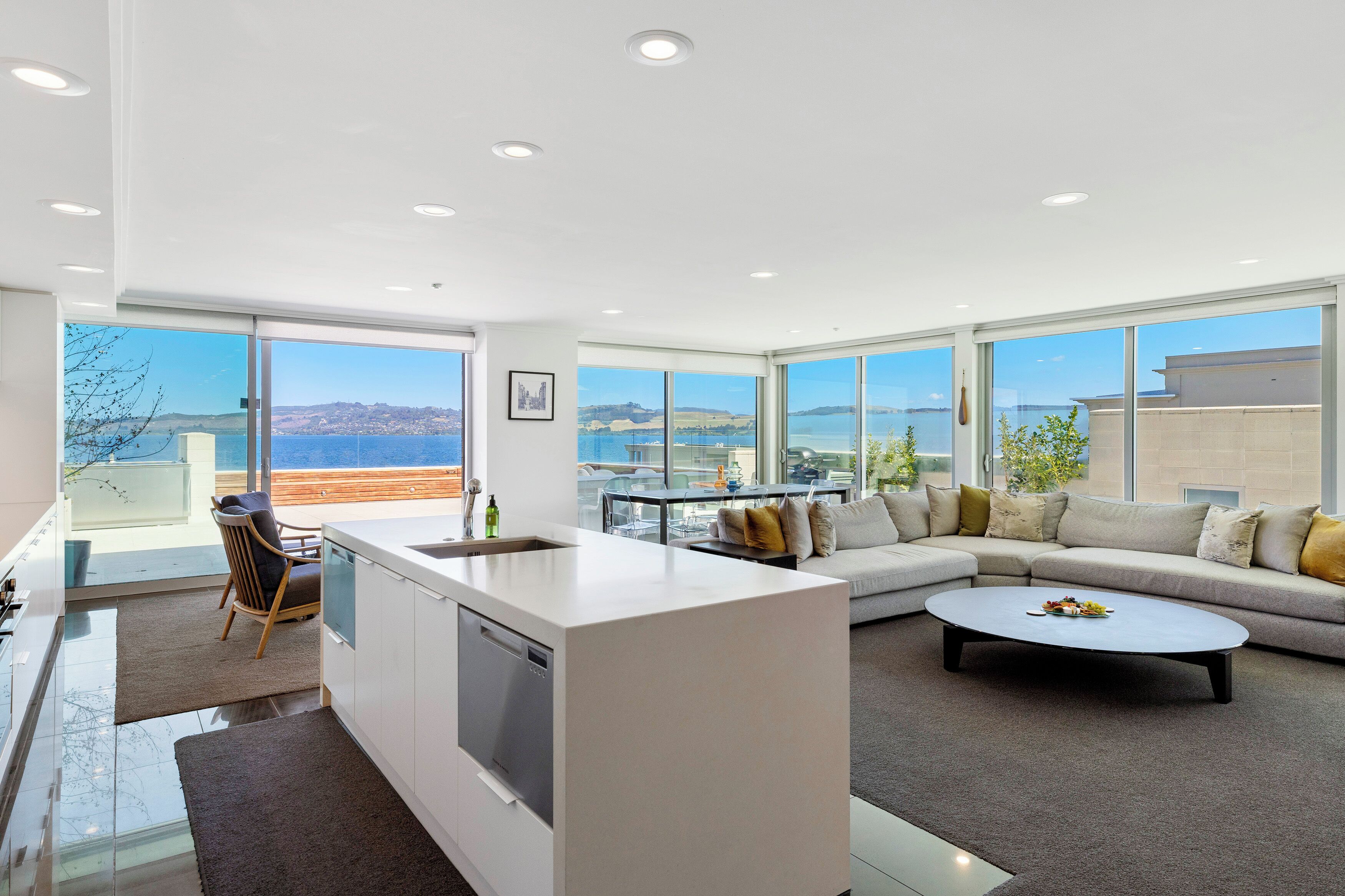 A modern living room with a large sofa, a coffee table, and a kitchen area with a dishwasher.