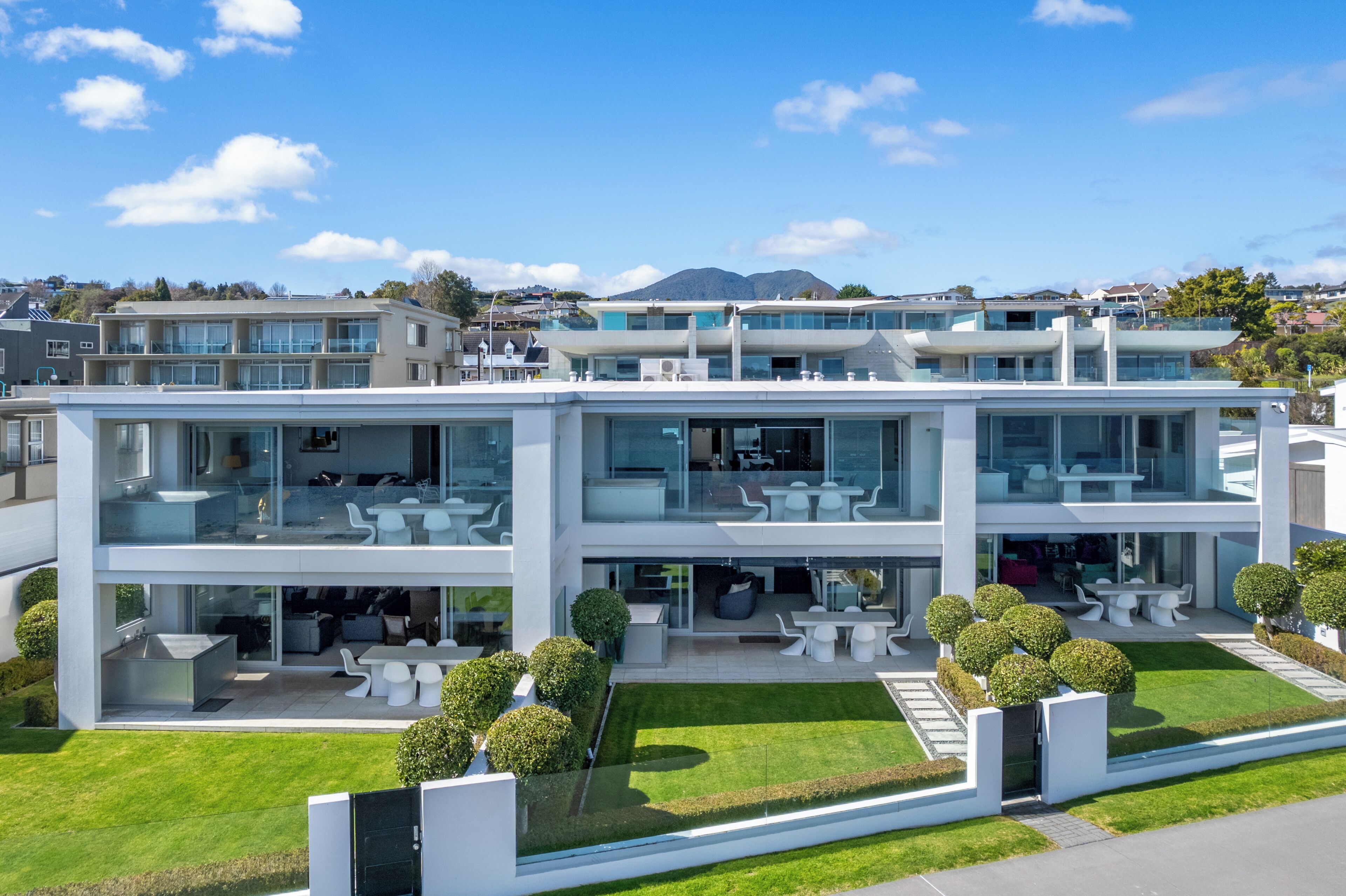 A modern two-story building with a glass facade, outdoor seating area, and a well-maintained lawn.