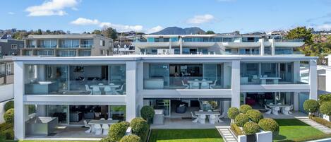 A modern two-story building with a glass facade, outdoor seating area, and a well-maintained lawn.