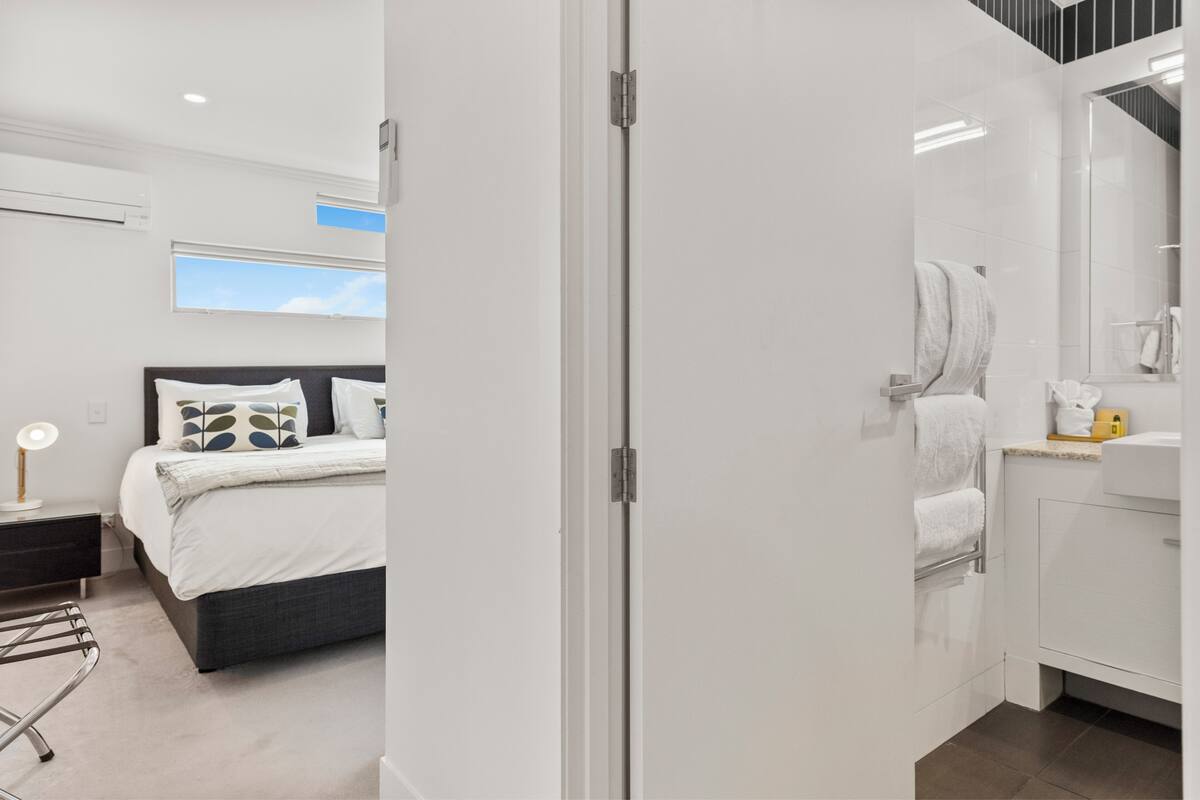 A modern hotel room with a bed, bedside table, and a bathroom with a sink and mirror.