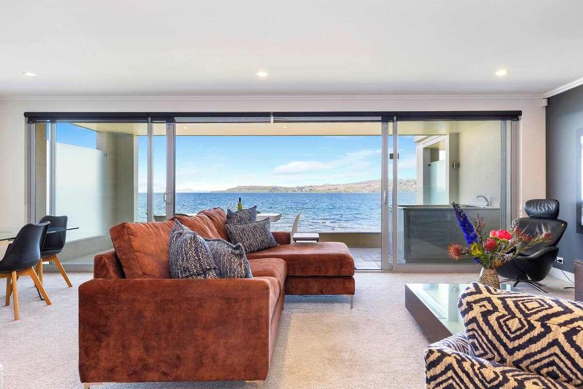 A modern living room with a sofa, chairs, a coffee table, and a view of the sea.