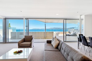 A modern living room with a glass wall, a sofa, a coffee table, and a view of the sea.