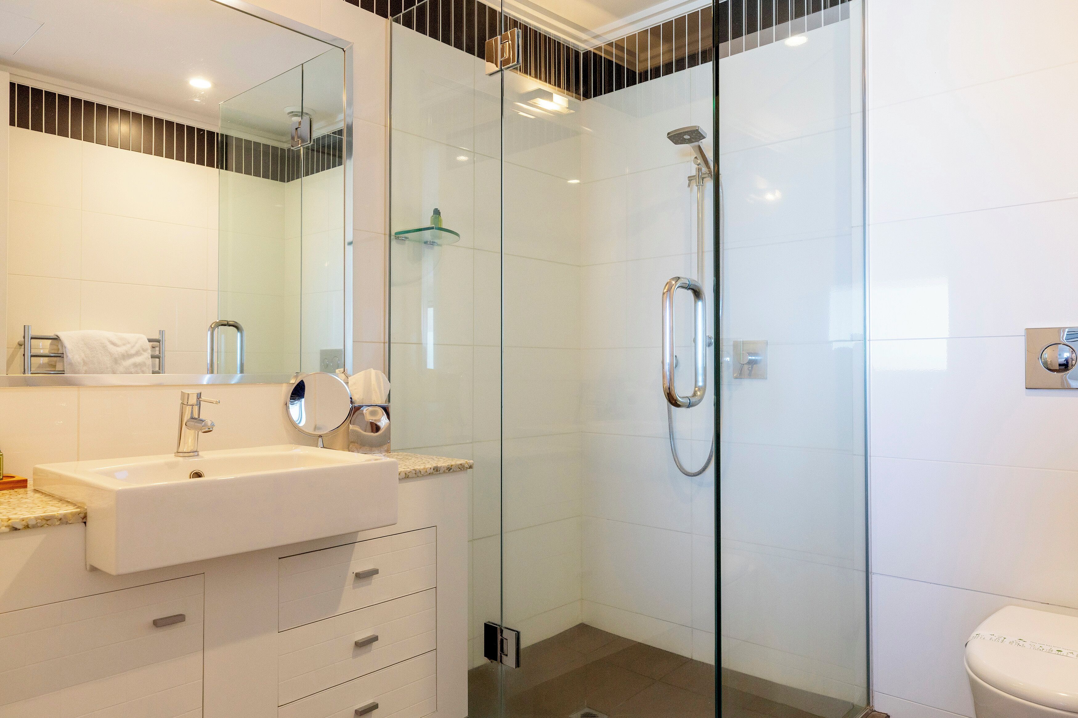 A modern bathroom with a glass-enclosed shower, a white sink, and a large mirror.