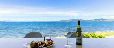 Una mesa con un plato de comida y una botella de vino, con vistas a una masa de agua.