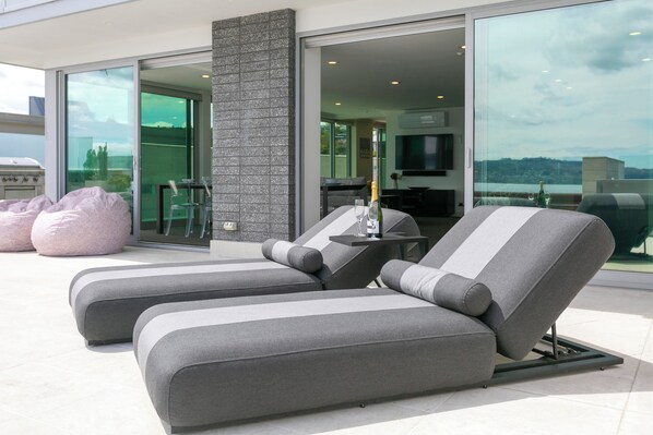 Un área de estar moderna al aire libre con dos sillones de descanso, una mesa, un pilar de piedra y vistas de la ciudad.