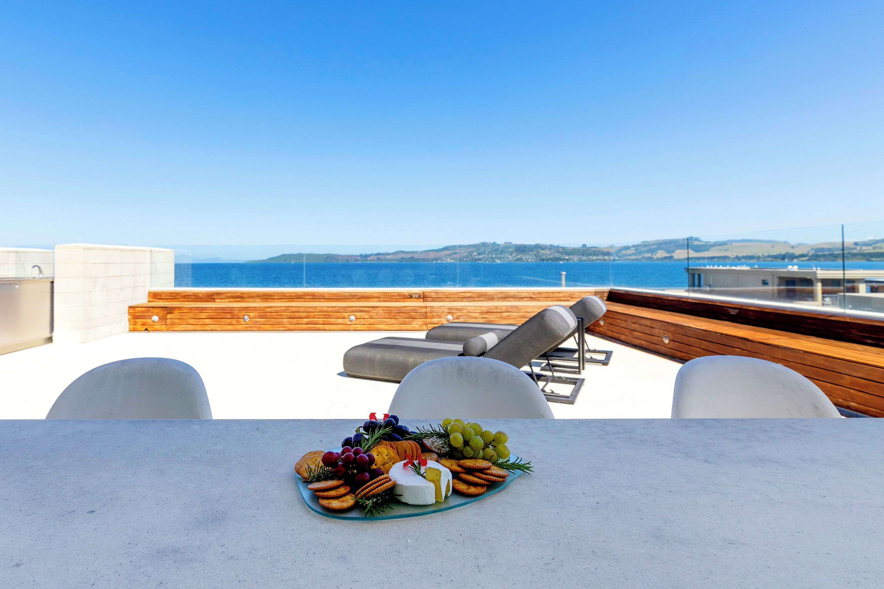 A terrace with a table set for a meal, overlooking a body of water and distant hills.