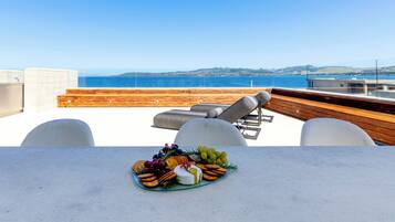 A terrace with a table set for a meal, overlooking a body of water and distant hills.