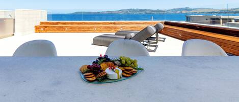 A terrace with a table set for a meal, overlooking a body of water and distant hills.