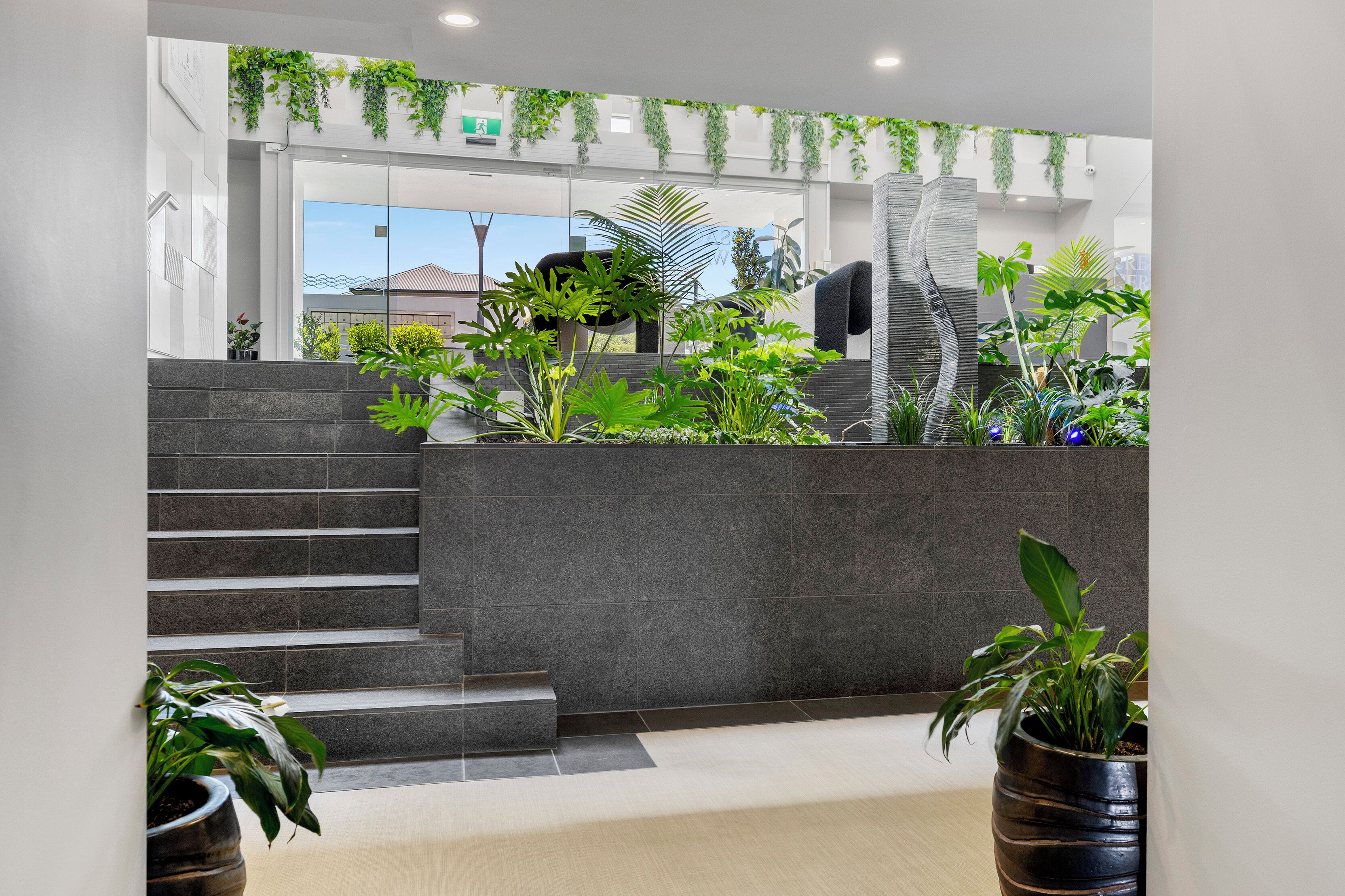 Un hall d’entrée moderne avec un escalier, des plantes en pot et une vue sur l’extérieur.