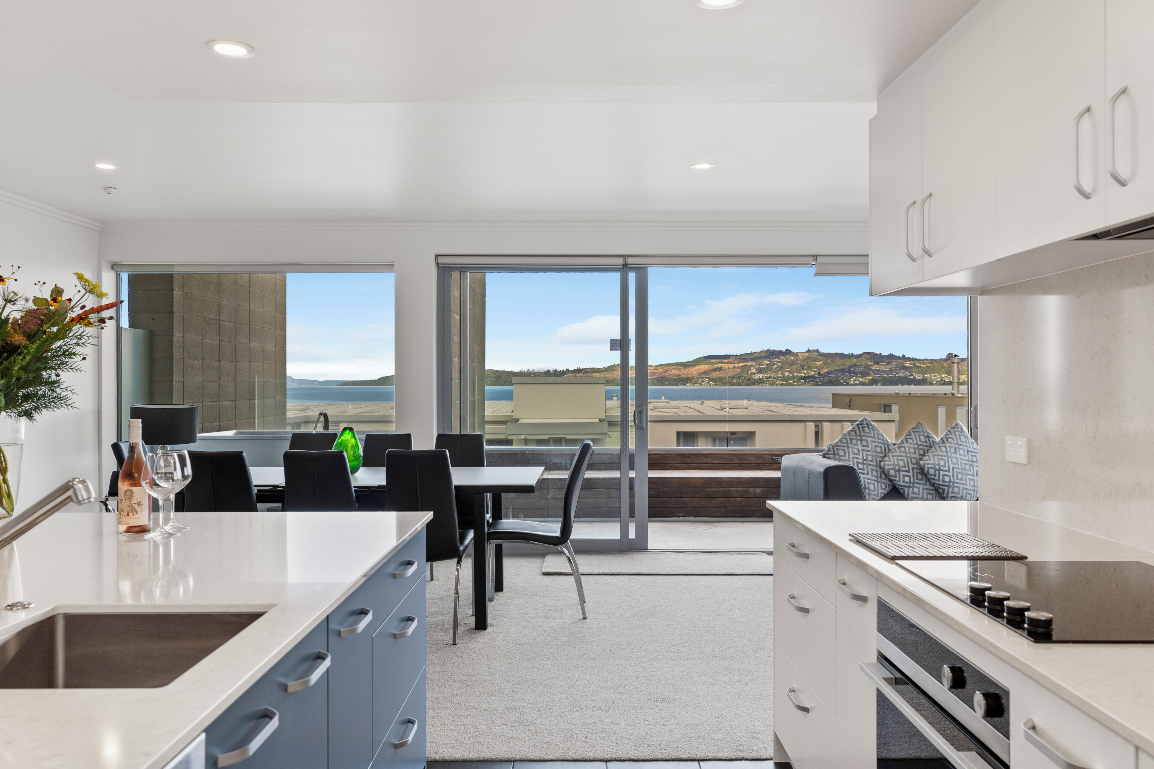 A modern kitchen with a large island, a dining area with a table and chairs, and a view of the landscape through large windows.