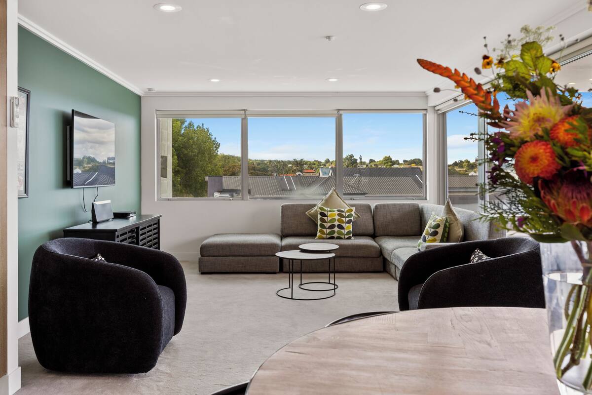 A modern living room with a sectional sofa, two armchairs, a coffee table, and a dining table.