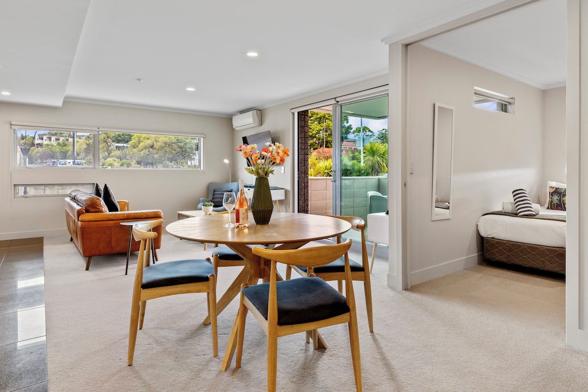 A modern living room with a dining table, chairs, a sofa, and a view of the outdoors.