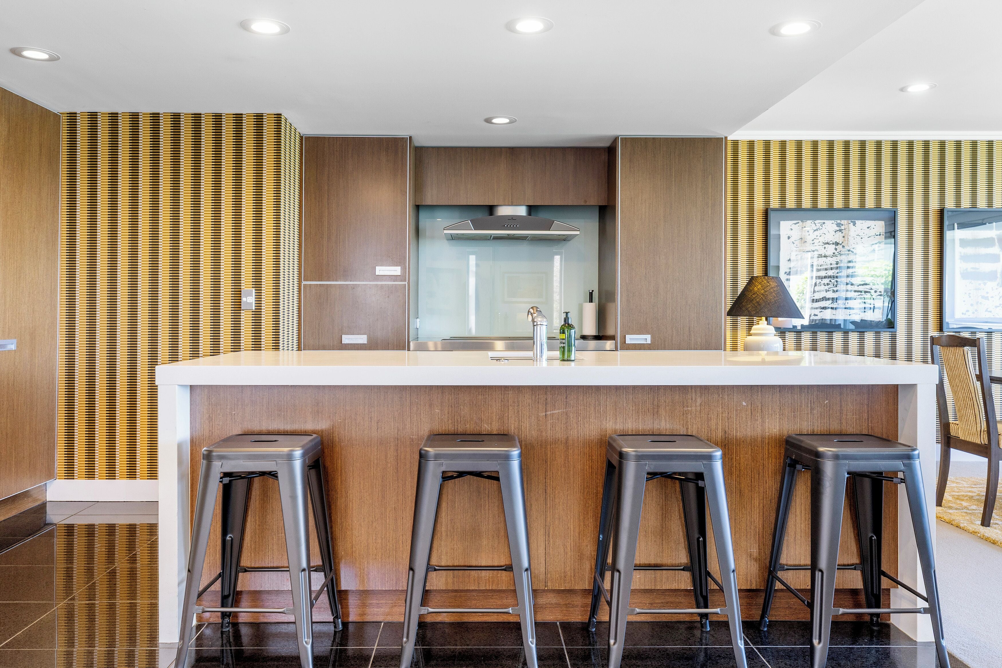 A modern kitchen with a central island, bar stools, and a large window.