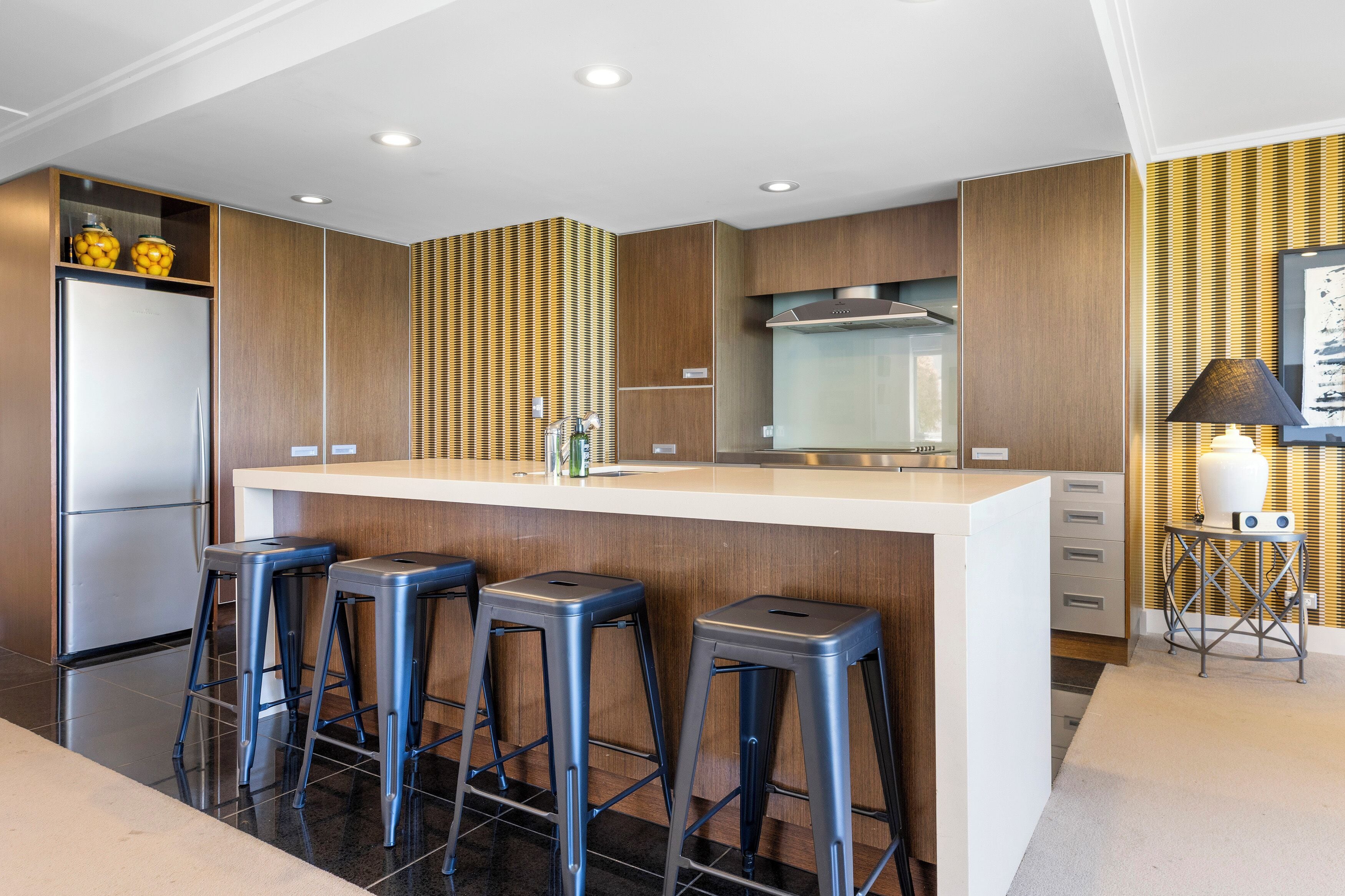 Una cocina moderna con una isla central, taburetes de bar, un refrigerador y una estufa.