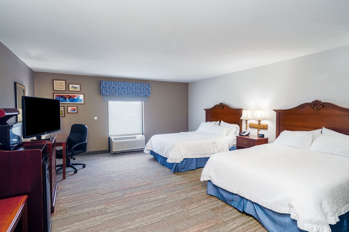 A hotel room with two beds, a desk with a TV, a chair, and a window with blinds.